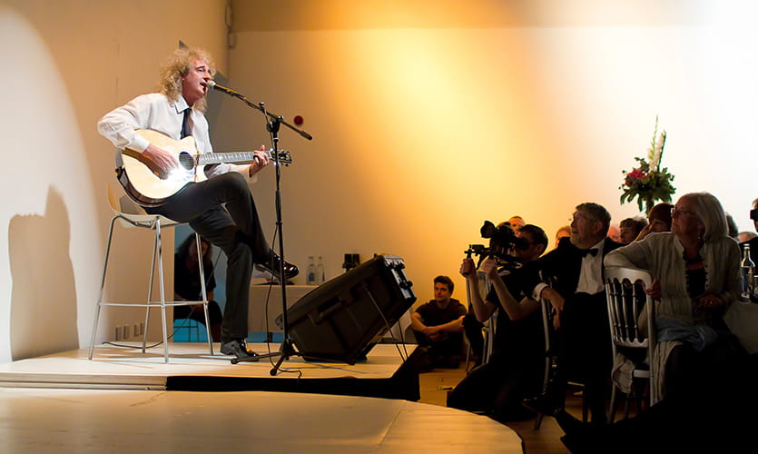 Brian sat on a stage playing guitar to an audience