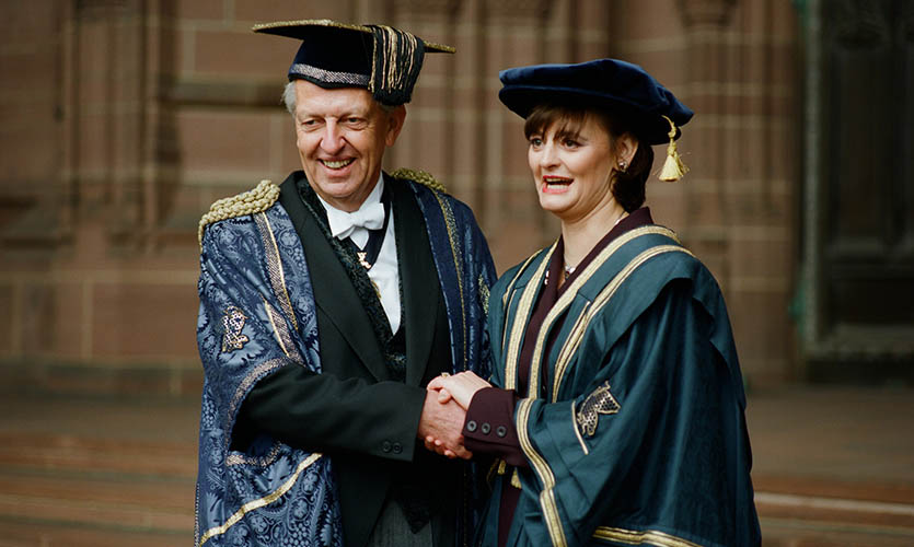 Cherie dressed in a cap and gown stood on the steps of the Anglican Cathedral shaking hands with a man