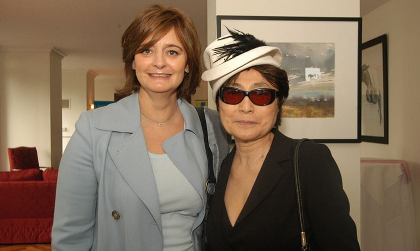 Cherie is smiling at the camera seen from the waist up stood next to Yoko Ono