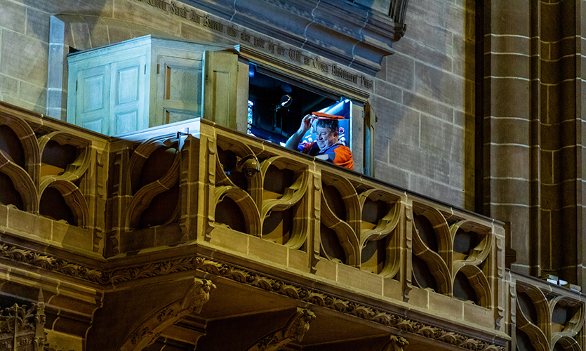 Ian is sat at the organ in the large stone building of the Anglican Cathedral just his head and shoulders can be seen from a far as he tilts his red cap in a gesture to the unseen audience below