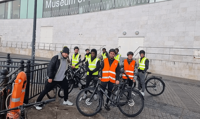Ibe stood to the left of a group of eight cyclists wearing high-vis vests stood behind bicycles outside of the Museum of Liverpool on the Pier Head
