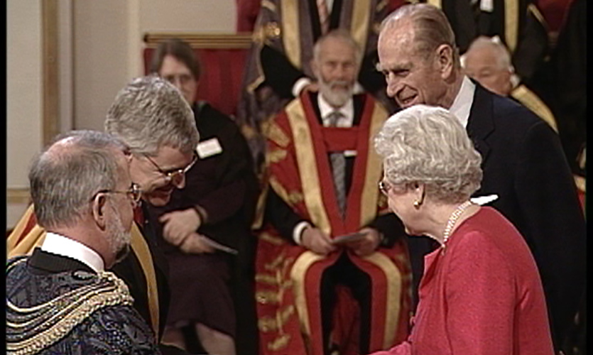 Mike dressed in robes shaking the hand of Queen Elizabeth the second 