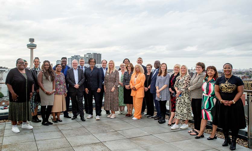 Moni pictured with ELT and leaders from across the Liverpool City region for the Leaders Reciprocal Mentoring Programme closing event with Liverpool city in the backdrop.