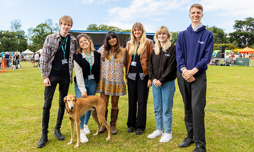 Nisha is stood in between five LJMU journalism students in a field at her charity dog show event, there is a dog stood to the left of Nisha’s feet
