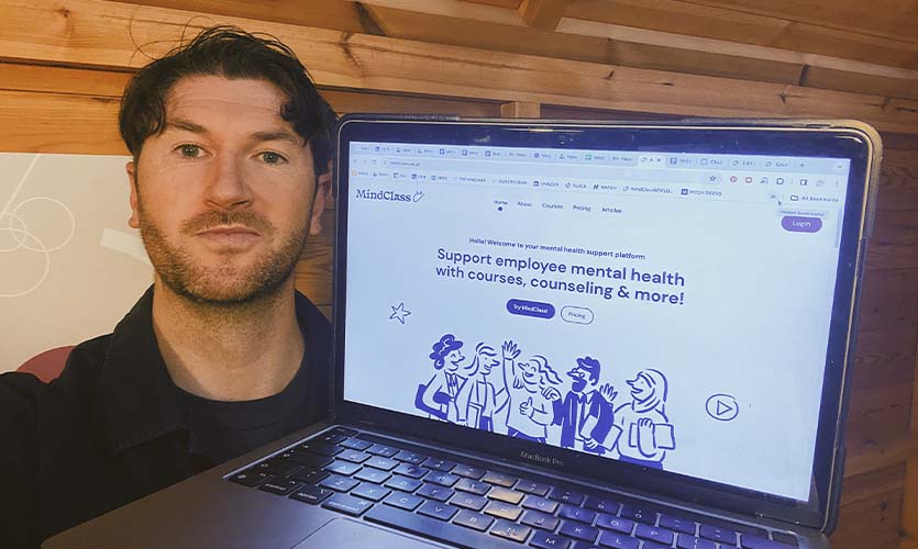 Phil holding an open laptop next to his face with a page from his mental health business website visible.