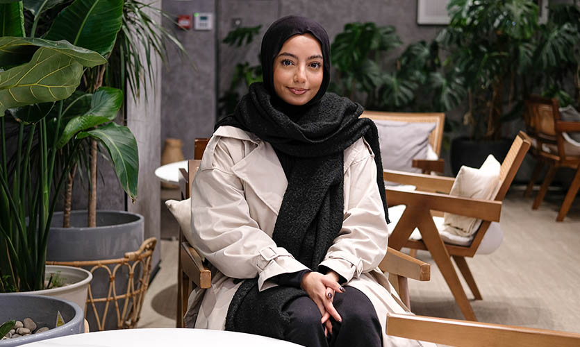 Selma sat down in a wooden chair wearing a beige mackintosh coat, black scalf and black hijab covering her hair