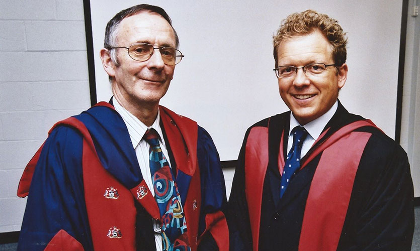 Tom stood on the left wearing graduation robes and Tim Cable stood to the right also wearing graduation robes