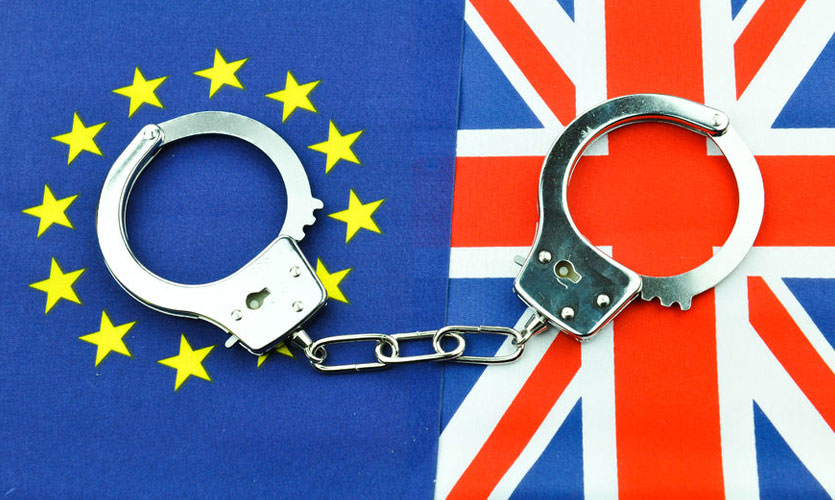 A pair of handcuffs on top of EU and British flags