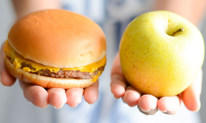Hands holding a cheeseburger and an apple