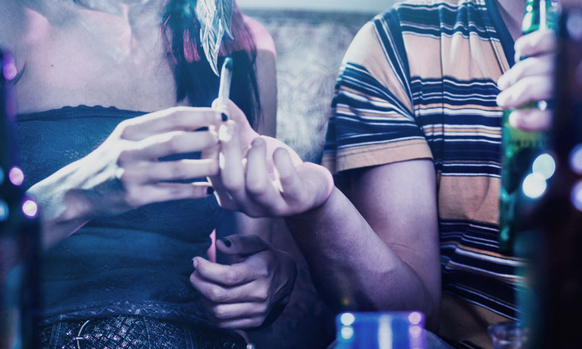 A man hands a marijuana joint to a woman at a party