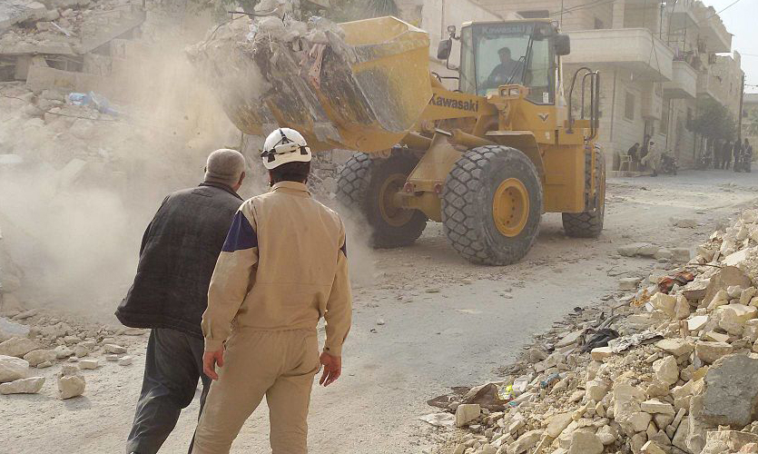Two emergency responders observe a bulldozer clearing rubble in Syria