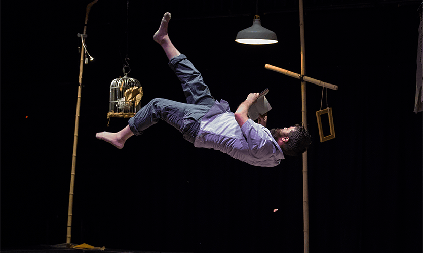 A man hanging horizontally on a stage whilst reading a book