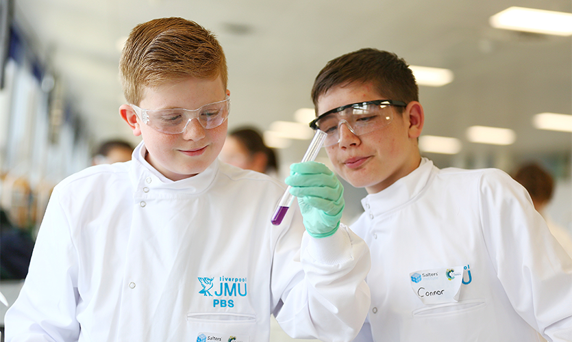 Two school students dressed in lab coats performing an experiment