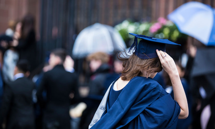 Student holding onto her mortarboard in rainy windy weather