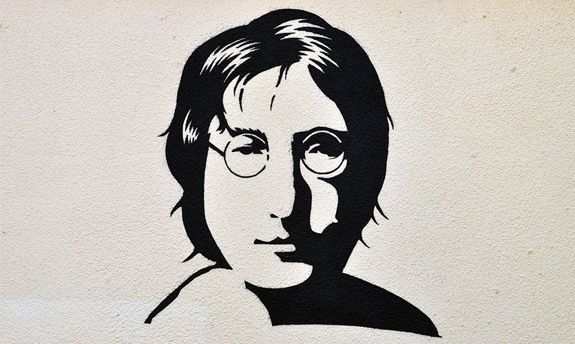 Black stenciled art work with John Lennon's face spray painted onto a white wall