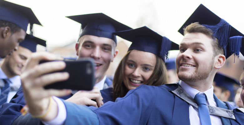 Image of graduates in cap and gown taking a selfie