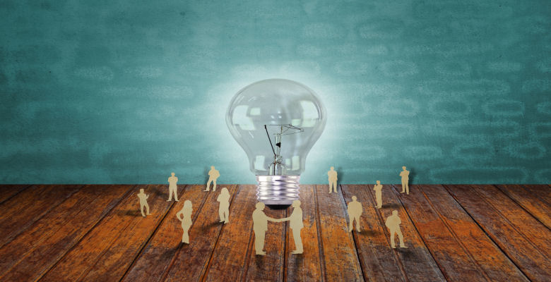 Image of a large lit light bulb with figures standing around it