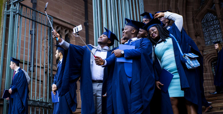 Image of graduates in cap and gown taking a selfie on Cathedral steps