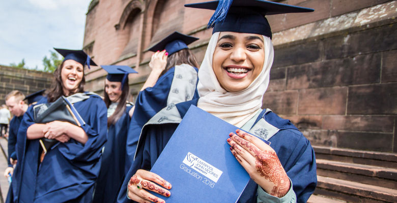 Image of female student in cap and gown holding brochure with henna on hands