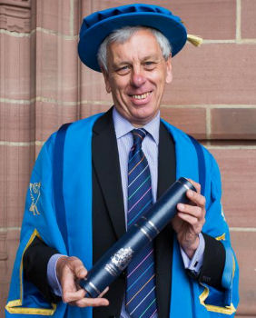 Image of John Cater in cap and gown with degree scroll receiving his Honorary Fellowship