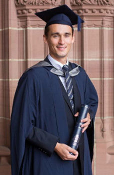 Image of Andrew Stevens-Davies in cap and gown with degree scroll