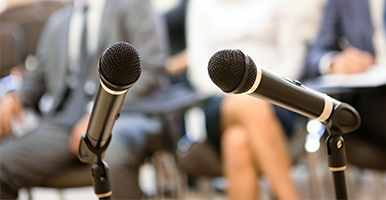 Image of two microphones on a podium with an audience in the background