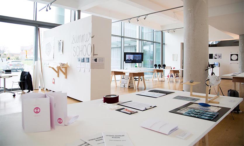 Image of the exhibition space with walls and tables filled with artwork.